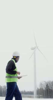 A Man in a Work Uniform is Diagnosing a Wind Turbine Using a Digital Tablet