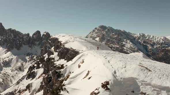 Cinematic circling drone shot of hiker standing on a steep snowy ridge