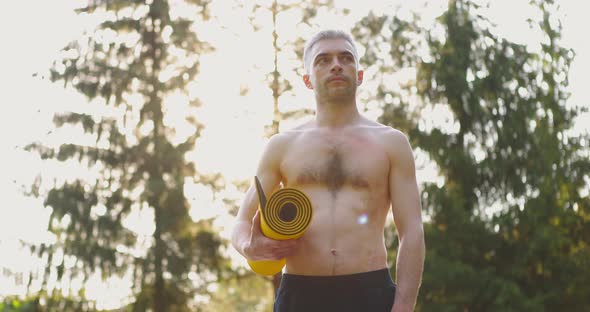 Pan Shot of Caucasian Sportsman Standing Outdoors with Yoga Mat in Hands Looking Away