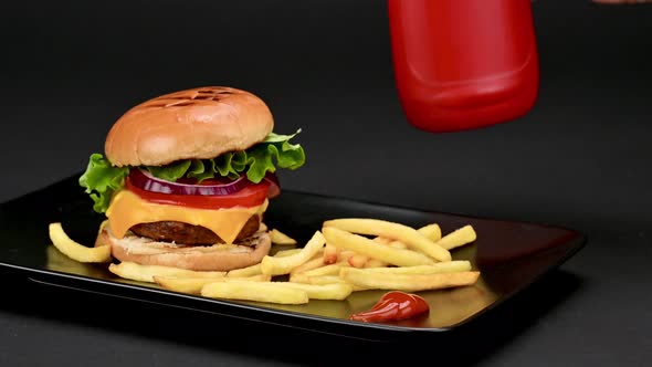 Delicious burger with fries and a woman's hand pouring ketchup