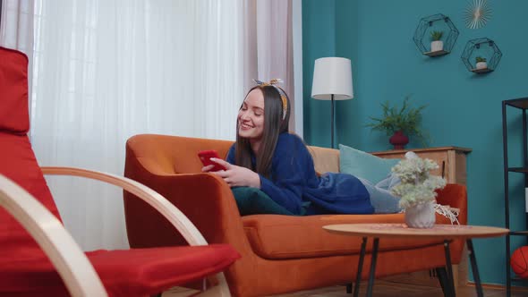 Relaxed Smiling Caucasian Young Woman Lying on Home Sofa with Smartphone Scrolling Browsing Online