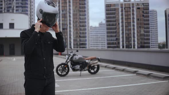Guy Wears Motorcycle Helmet on Top of the Parking in Front of Motorbike