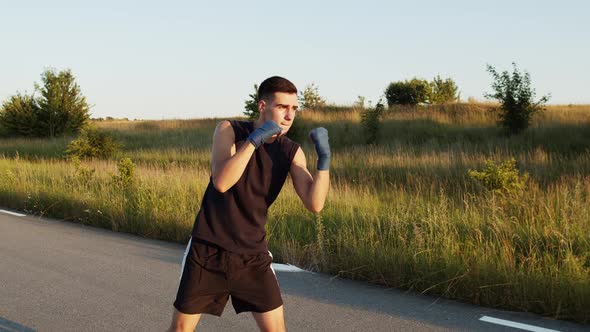Kickboxer with Wrapped Hands in Boxing Tapes Training Kicks Outdoors