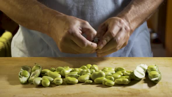 Wide, slider shot from left to right of a cutting board with shelled fava beans on the board and a m