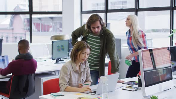 Diverse business people using laptops going through paperwork in modern office