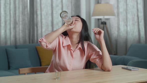 Drunk, Depressed Asian Woman With Smartphone On Table Drinking Vodka From The Bottle At Home