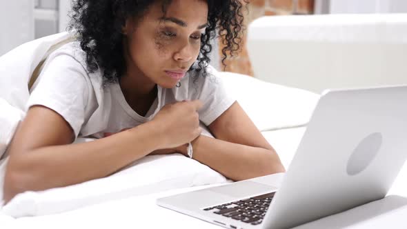 Upset AfroAmerican Woman in Bed Working on Laptop and Reacting to Loss