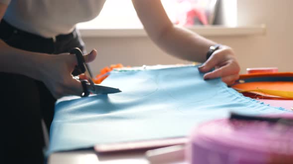 Seamstress Cuts Blue Fabric Piece with Scissors on Desk