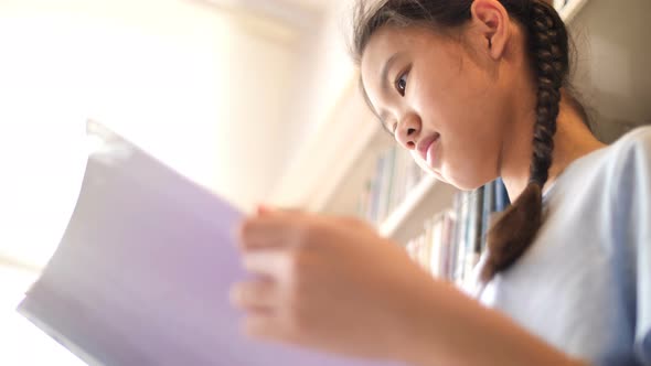 Asian teenager student reading a book in school library.