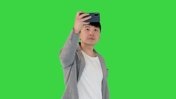 Young Asian Man Walks Makes a Photo and Smiles on a Green Screen Chroma Key