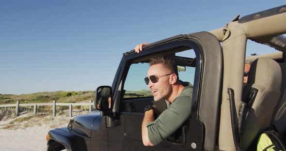 Happy caucasian man in sunglasses getting out of car on sunny day at the beach