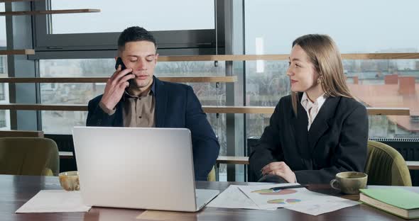 Man Talking the Phone and a Woman Watching From the Side in the Brightly Lit Modern Office