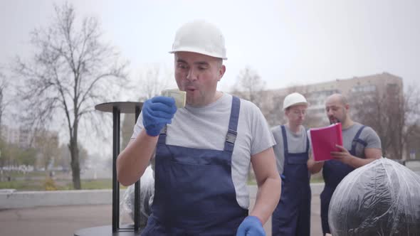 Portrait of Glad Caucasian Man in White Helmet and Blue Uniform Listening To Money Rustle