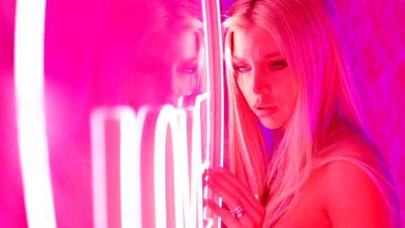 Portrait of a Blonde Beauty in a Pink Room with Neon Light Stands Against the Wall