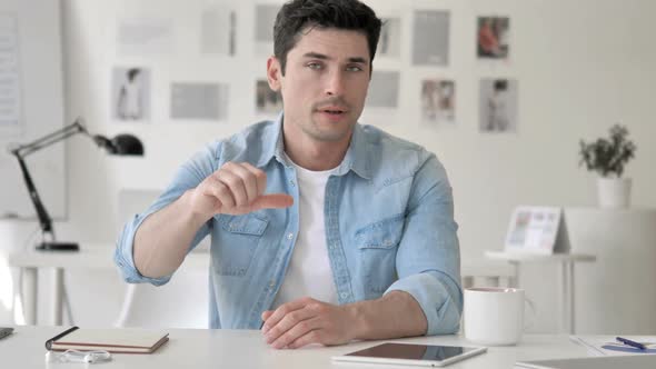 Thumbs Down By Casual Young Man Sitting at Workplace