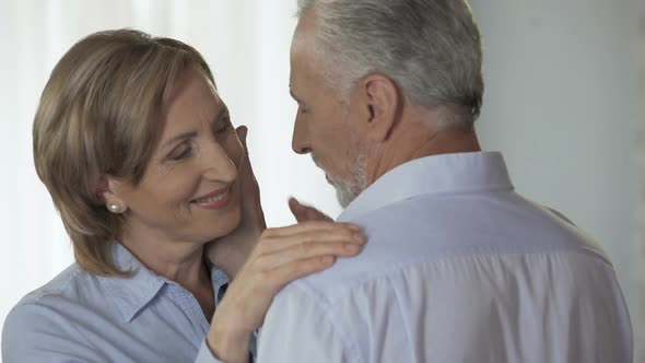 Retiree woman looking at husband, man cupping her cheek, happy late adulthood