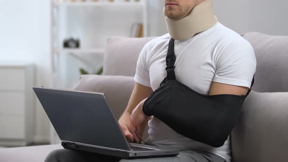 Man in Arm Sling and Cervical Collar Working on Laptop at Home, Trauma Treatment