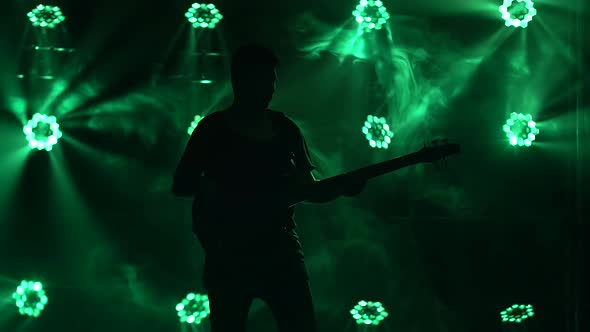 Silhouette of a Young Guy Playing on the Electric Guitar on Stage in a Dark Studio with Smoke and