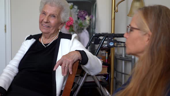 As blonde mature woman talks, an elderly woman smiles and looks toward her.