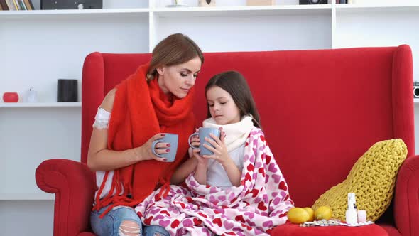 Mother and Daughter Sitting on Red Couch and Drinking Tea