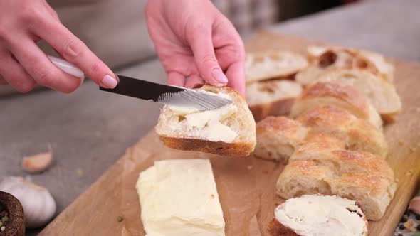 Woman Smearing Soft Butter on Slice of Baguette Bread By Knife at Domestic Kitchen