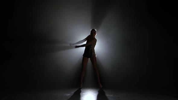 Girl Gymnast with Mace in Hand Revolve Around Him. Black Background. Light Rear. Silhouette