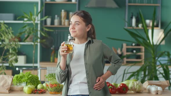 Happy Young Woman Enjoying Freshsqueezed Juice Using Organic Products in Modern Kitchen