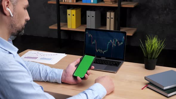 Man Broker Scrolling Green Screen Smartphone Laptop with Stock Exchange Chart