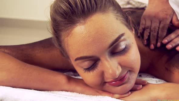 Relaxed Woman Lying on Spa Bed for Body Scrubbing Massage Using Traditional Herb