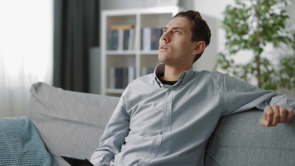 Thoughtful Man Sitting on Couch with Tablet