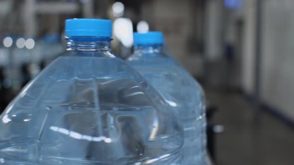 Close-up of five-liter bottles traveling on a conveyor belt from the camera