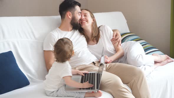 Little Kid Working on Laptop, While Cheerful Parents Looking at Each Other