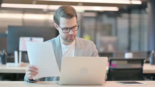 Man with Laptop Reading Documents in Office