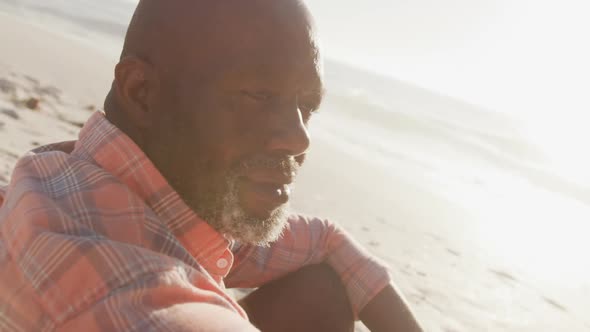 Senior african american man wearing shirt and sitting on sunny beach