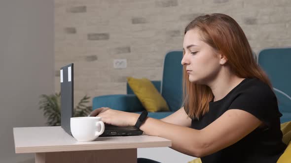 Young Woman Is Drinking a Cup of Coffee While Is Working at the Laptop From Home Office.