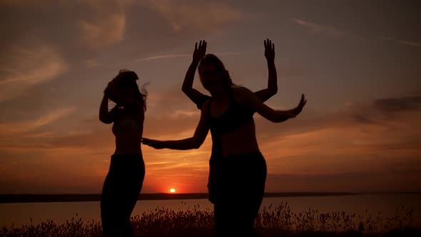 Silhouettes of Friends Dancing Rejoicing in Field at Sunrise