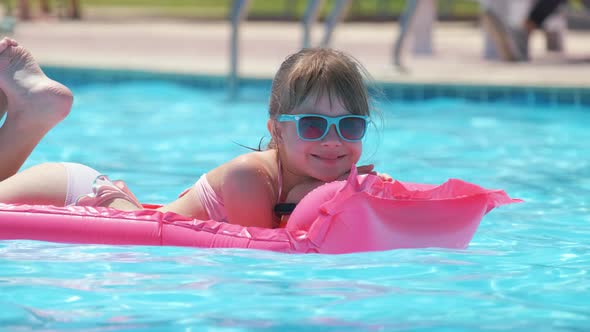 Happy Child Girl Relaxing on Inflatable Air Mattress in Swimming Pool on Sunny Summer Day During