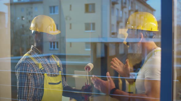 View Through Window of African Builder and Caucasian Foreman Discussing Equipment for Renovation