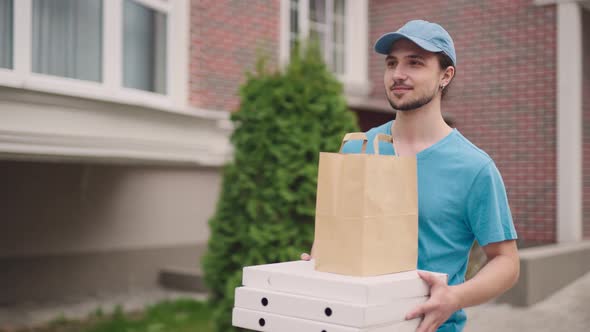 A Young Food Delivery Man Walks Through a Modern Pleasant Neighborhood