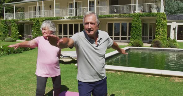 Happy caucasian senior couple practicing yoga in garden standing and stretching in the sun
