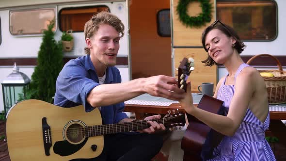 Bearded Guy Teaching Her Girlfriend Play the Guitar Outdoors Sitting Close to Their Trailer House