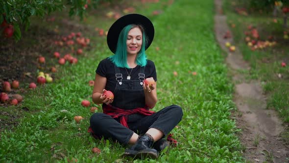 Blue Haired Hipster Woman Sitting and Juggles Ripe Red Apples in Garden at Autumn Season. Cheerful