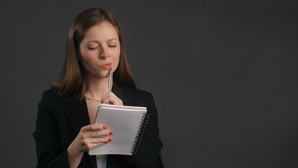 Young Woman in Black Suit Smiles and Writes Her Ideas to the Paper Notepad Making the Notes with