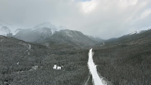 Drone approaching road through the forest at the foot of the beautiful mountains in Alberta, Canada