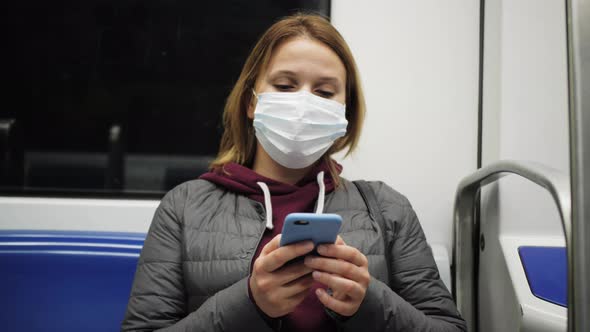 Young Woman in Protective Medical Face Mask in a Subway Train Using Mobile