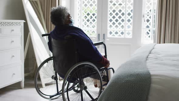 Senior african american woman wearing face mask sitting on the wheelchair at home