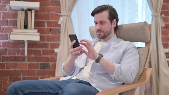 Casual Young Man Having Success on Smartphone at Home