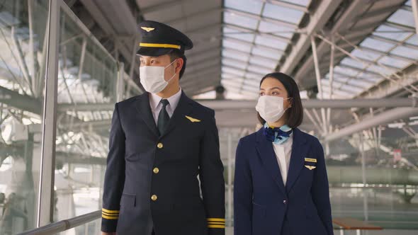 Airliner pilot and air hostess wearing face mask walking in airport terminal to the airplane.