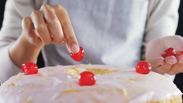 Woman topping a fresh baked cake with cherry