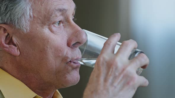 Close Up Senior Old Mature Caucasian Man Looking Away Thinking Holding Glass of Clean Still Water
